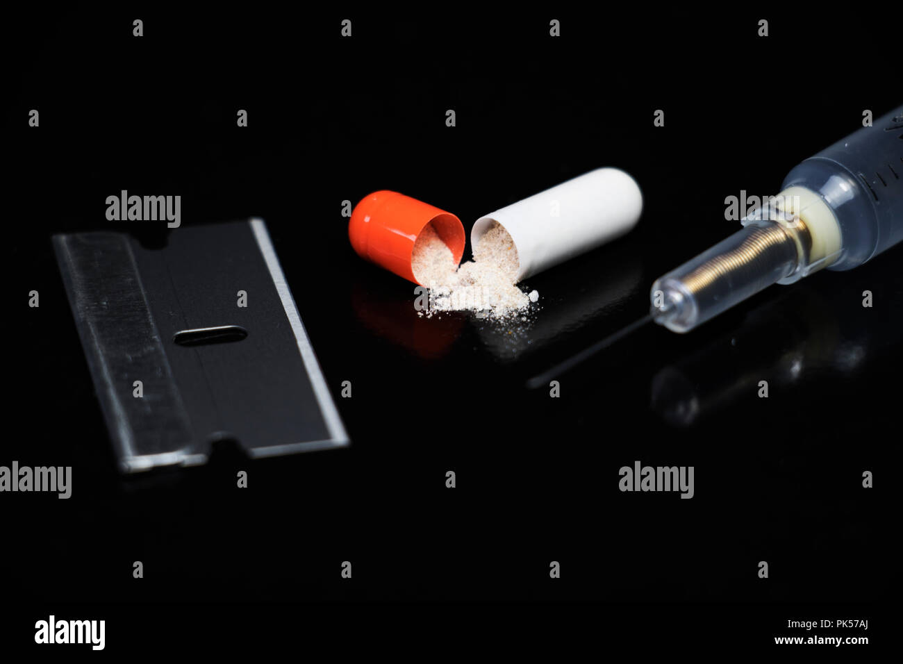 Drug addiction. Big Pharma, Healthcare industry. Razor blade, pills, and syringes. Drug paraphernalia isolated on black background. Medical objects. Stock Photo