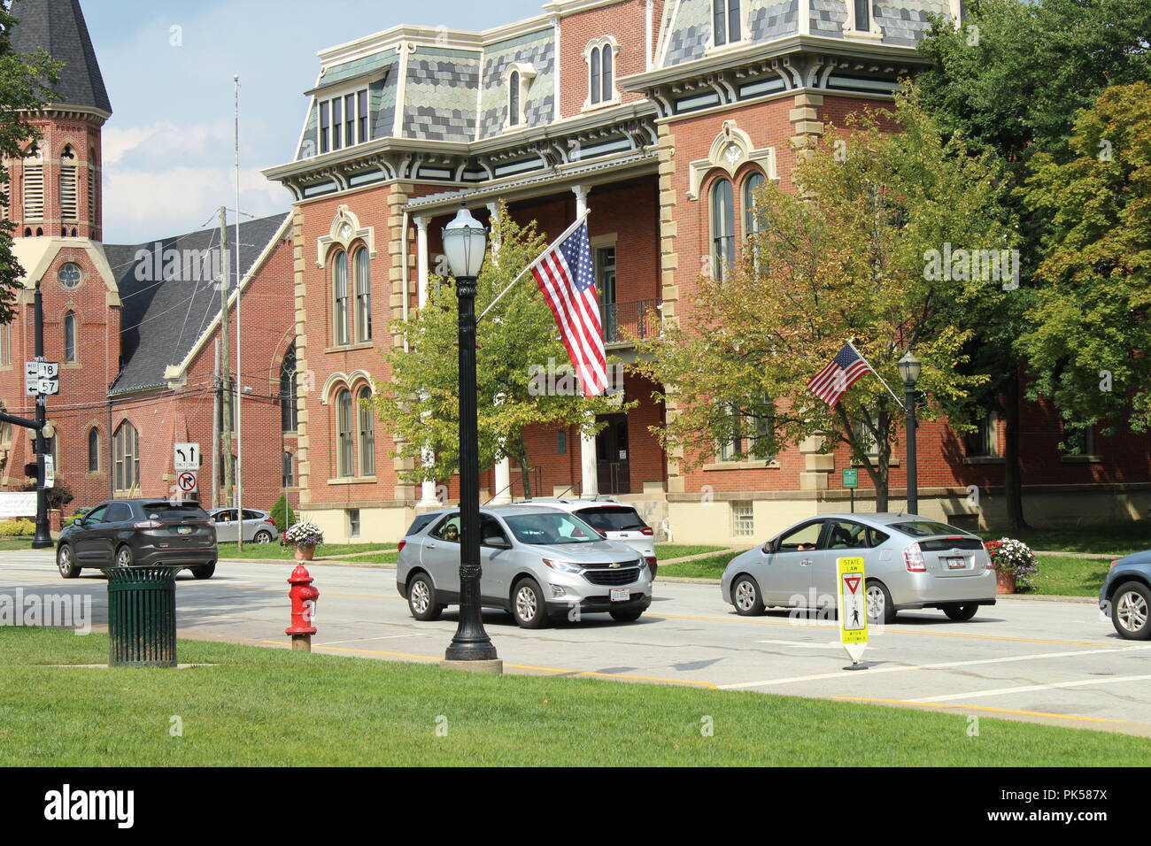 big brick building in a small rural town with traffic on the street with a flag and light pole Stock Photo