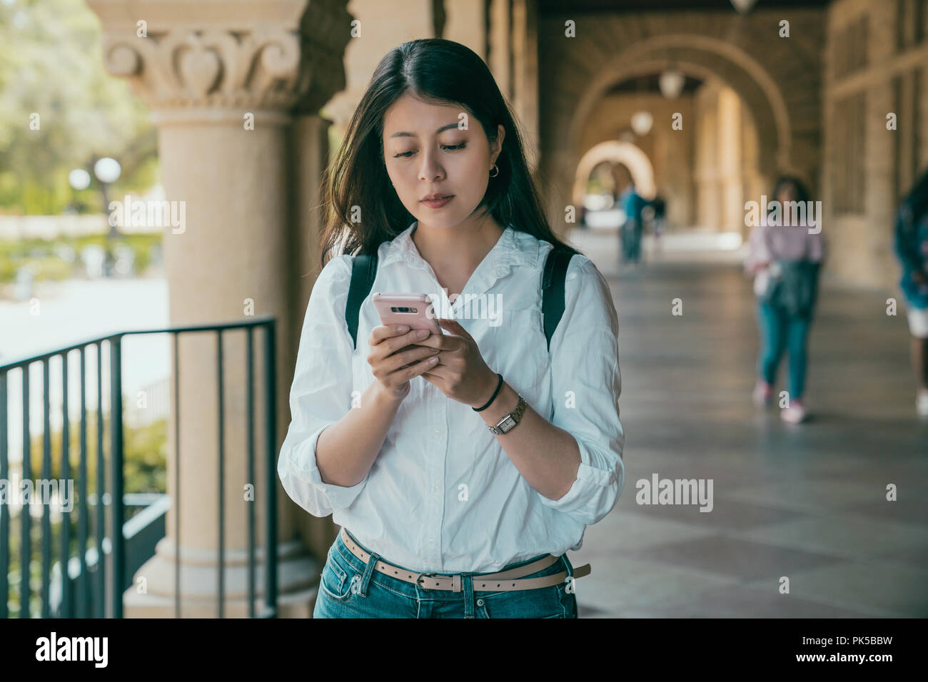 young beautiful student holding her phone and texting her friends for where they are heading to. Stock Photo