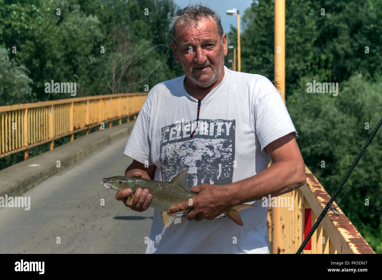 Samac, Bosnia and Herzegovina, August 2018 - Angler on a bridge holding a Barbel (Barbus barbus) that has just been caught from the River Bosna Stock Photo