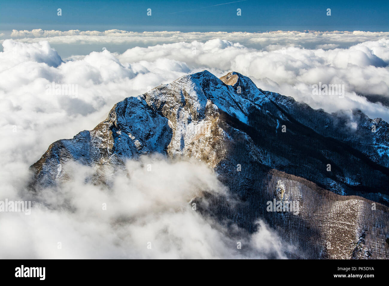 Tuscany Mount Corchia, pictured here by the summit of the Pania della Croce, sprinkled with snow emerges as an island with clouds covering the Tuscan coast. In recent years, due to climate change, snowfall on the Apuan chain has been quite scarce. Stock Photo