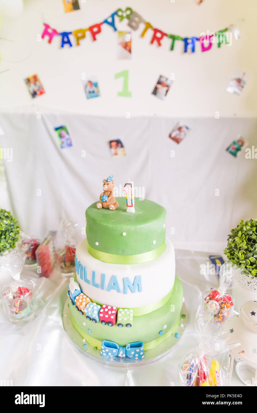 Green and White Birthday Cake with One Year Old Candle with Happy Birthday Banner in the Background Stock Photo