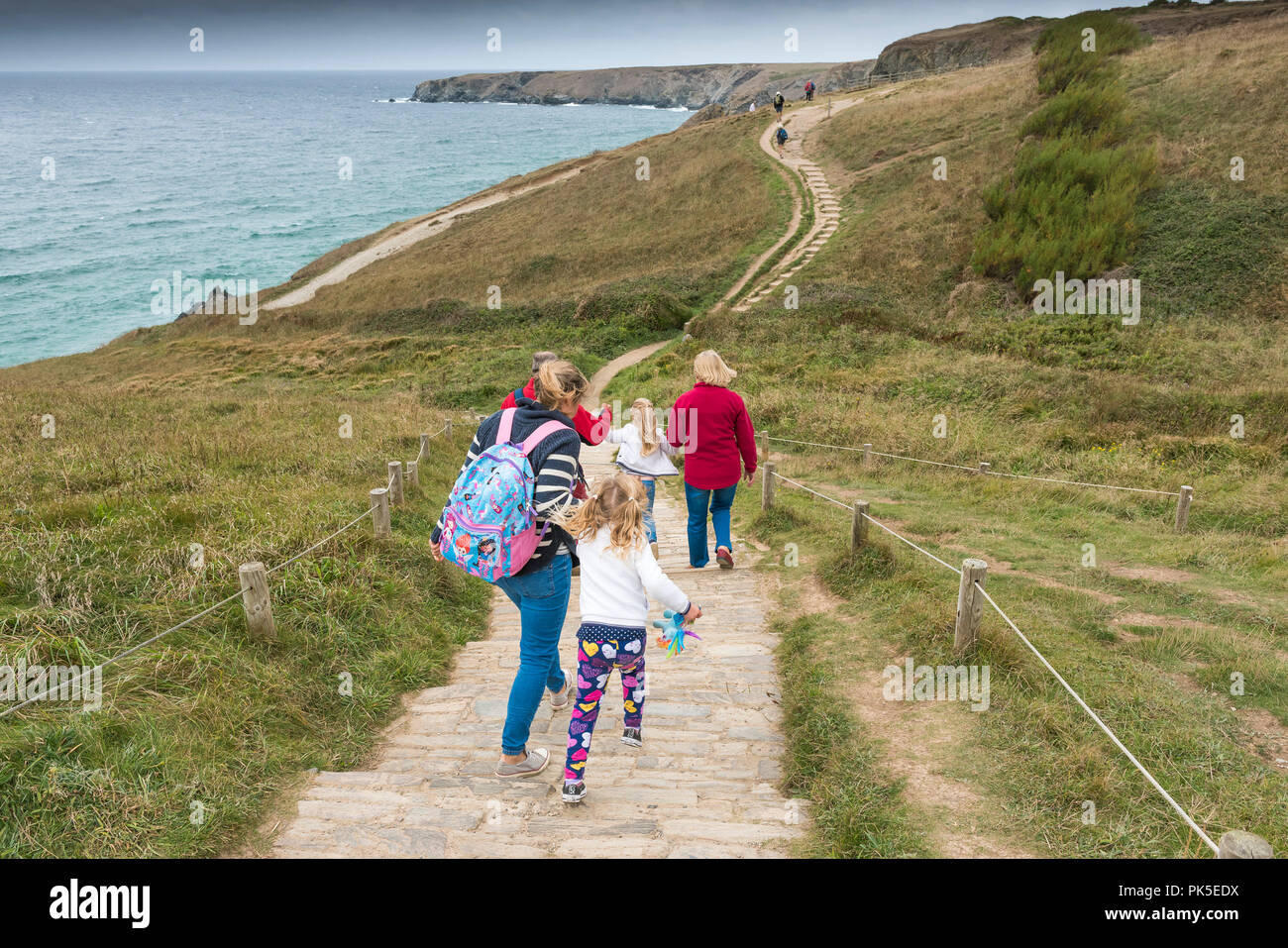 A family of holidaymakers walking down the South West Coast Path to Bedruthan Steps in Cornwall. Stock Photo