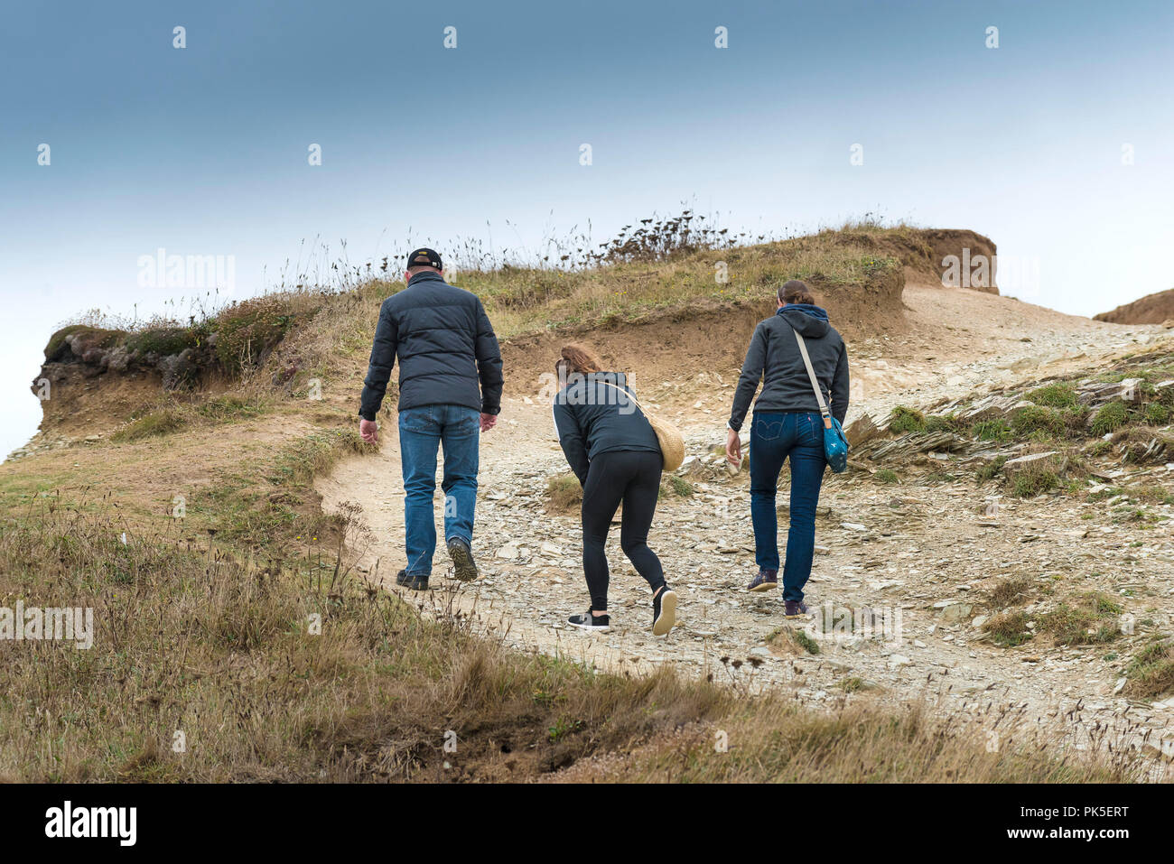 Three people walking along a heavily eroded worn footpath on the coast of Cornwall. Stock Photo