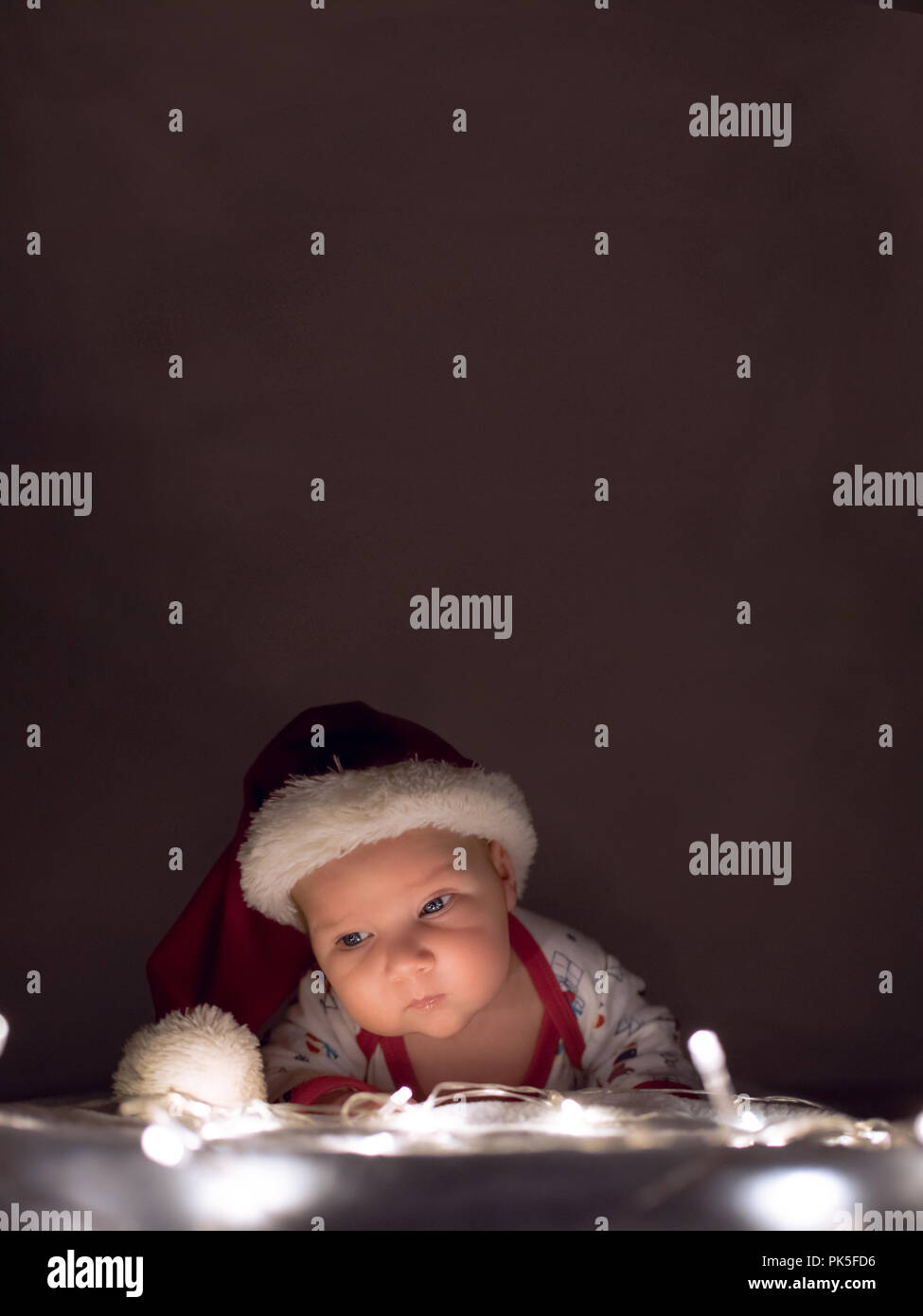 Christmas poster. Newborn baby with Santa hat lying on Christmas lights. Overhead space for text or other elements. Stock Photo