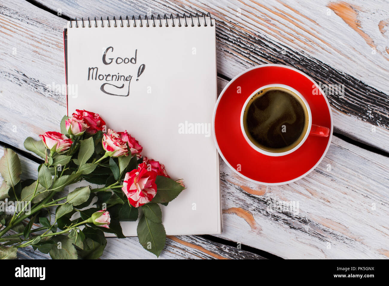 Cup of coffee, hybrid rose flowers and good morning note. Flat lay ...