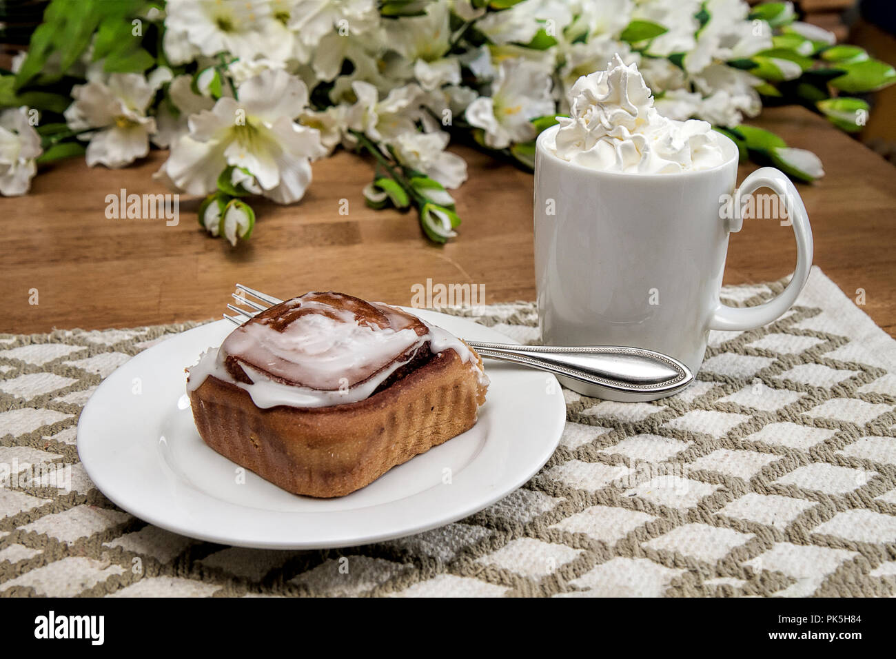 Hot chocolate loaded with whipped cream.  Flow blue dishes.  Large frosted danish all on kitchen table with window background and flowers. Stock Photo