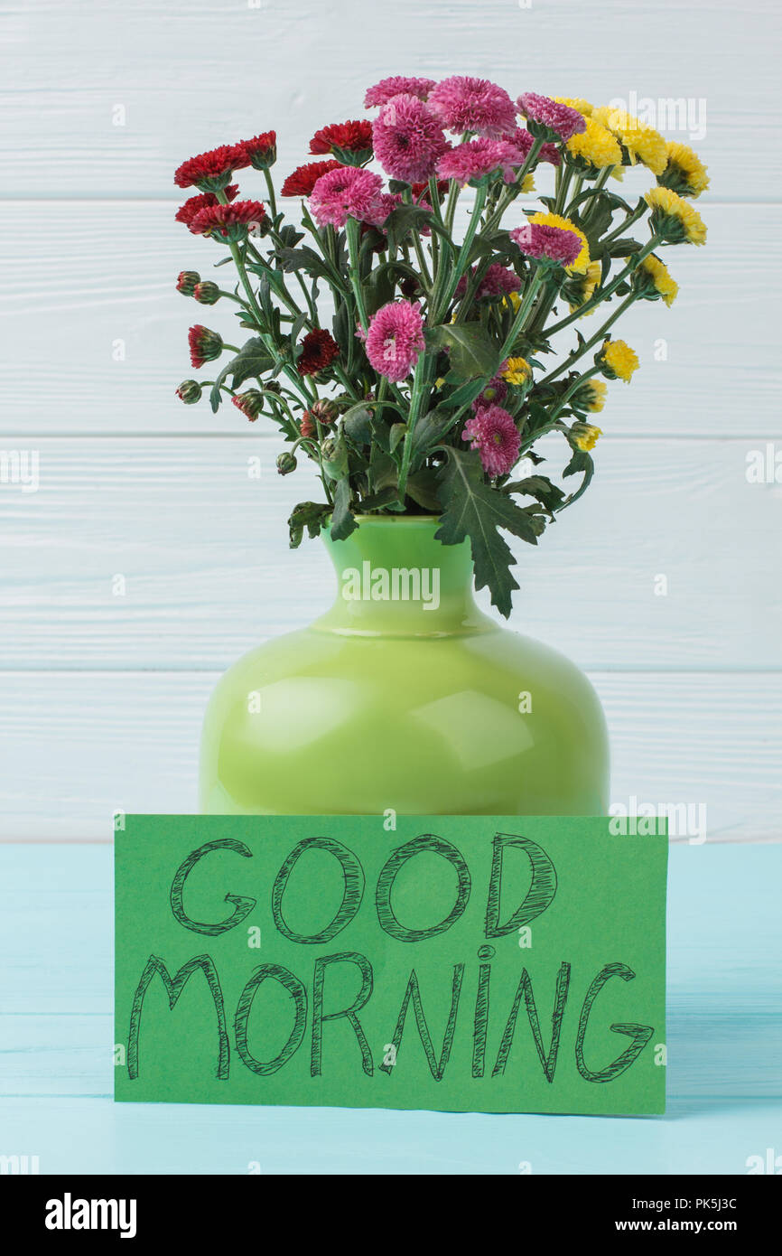 Flowers morning surprise concept. Bouquet of chrysanthemum flowers in a green ceramic vase. Light blue wooden background. Stock Photo