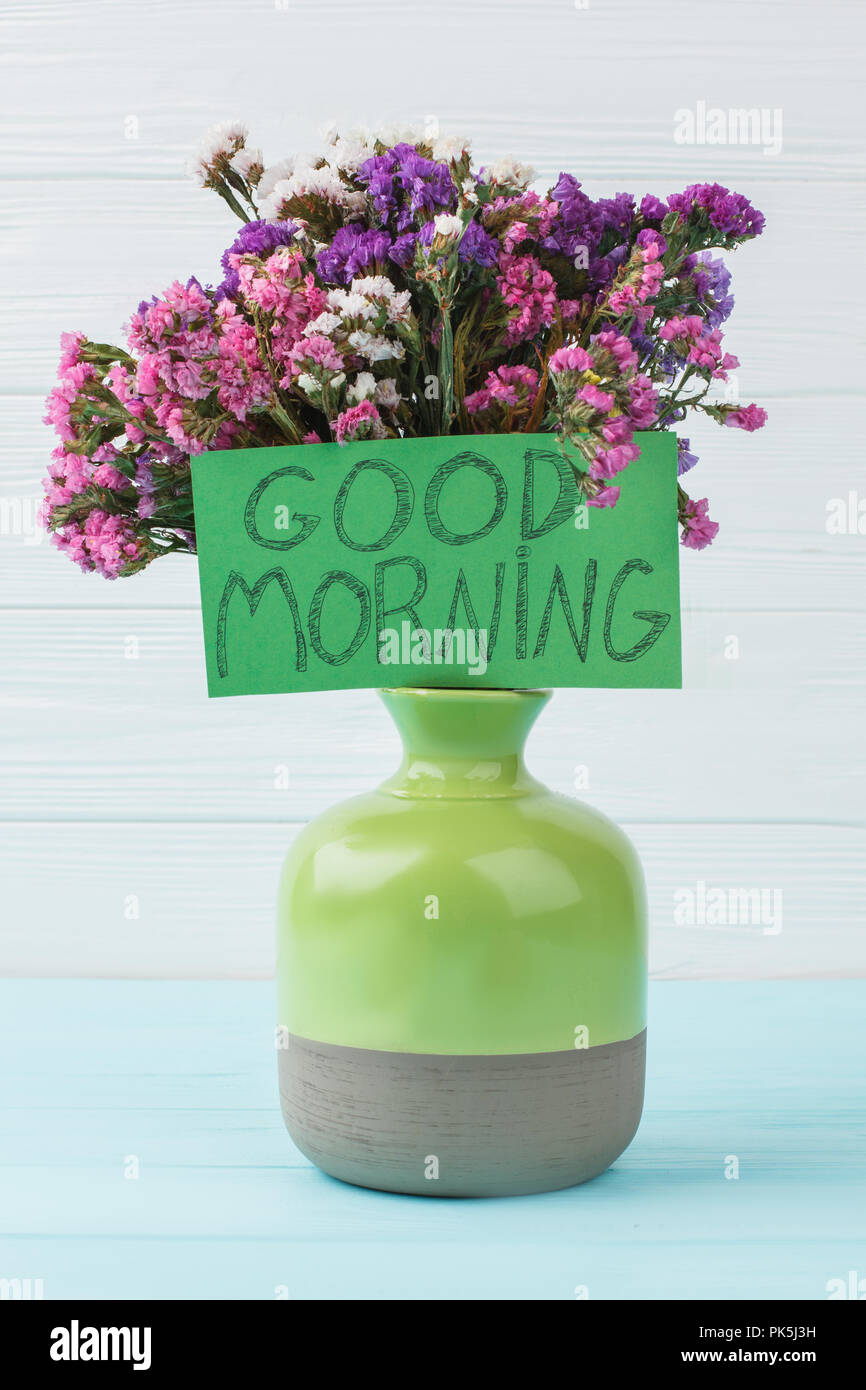 Green vase with flowers. Good morning wish, pleasant surprise for mother. Blue wooden background. Stock Photo