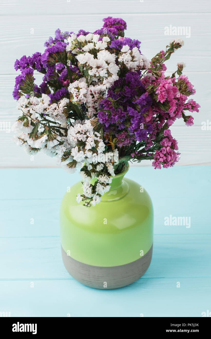 Multicolored statice limonium flowers in a green ceramic vase. Blue wooden background. Stock Photo