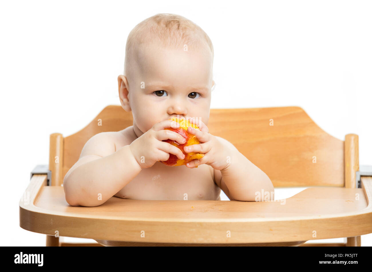 Cute baby girl eating peach while sitting in high chair over white background Stock Photo