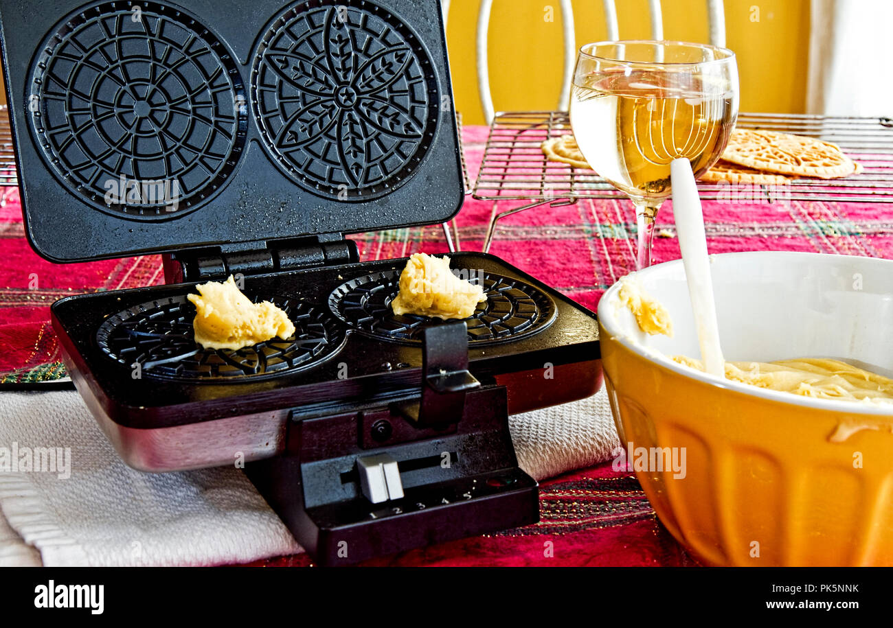 Italian Pizzelles being made in kitchen with ingredients and wine glass by bowl of batter. Stock Photo