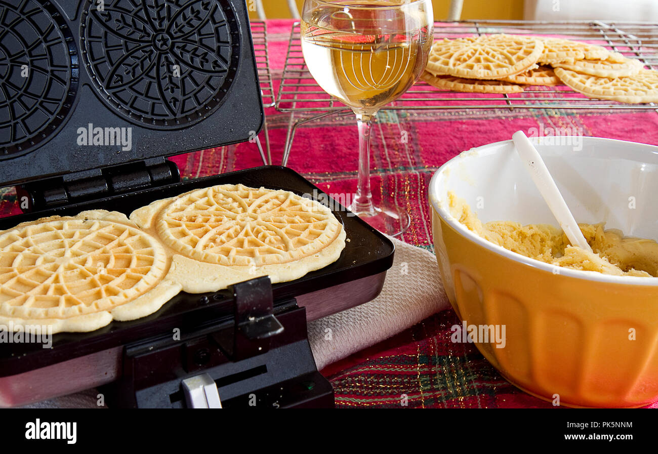 Italian Pizzelles being made in kitchen with ingredients and wine glass by bowl of batter. Stock Photo