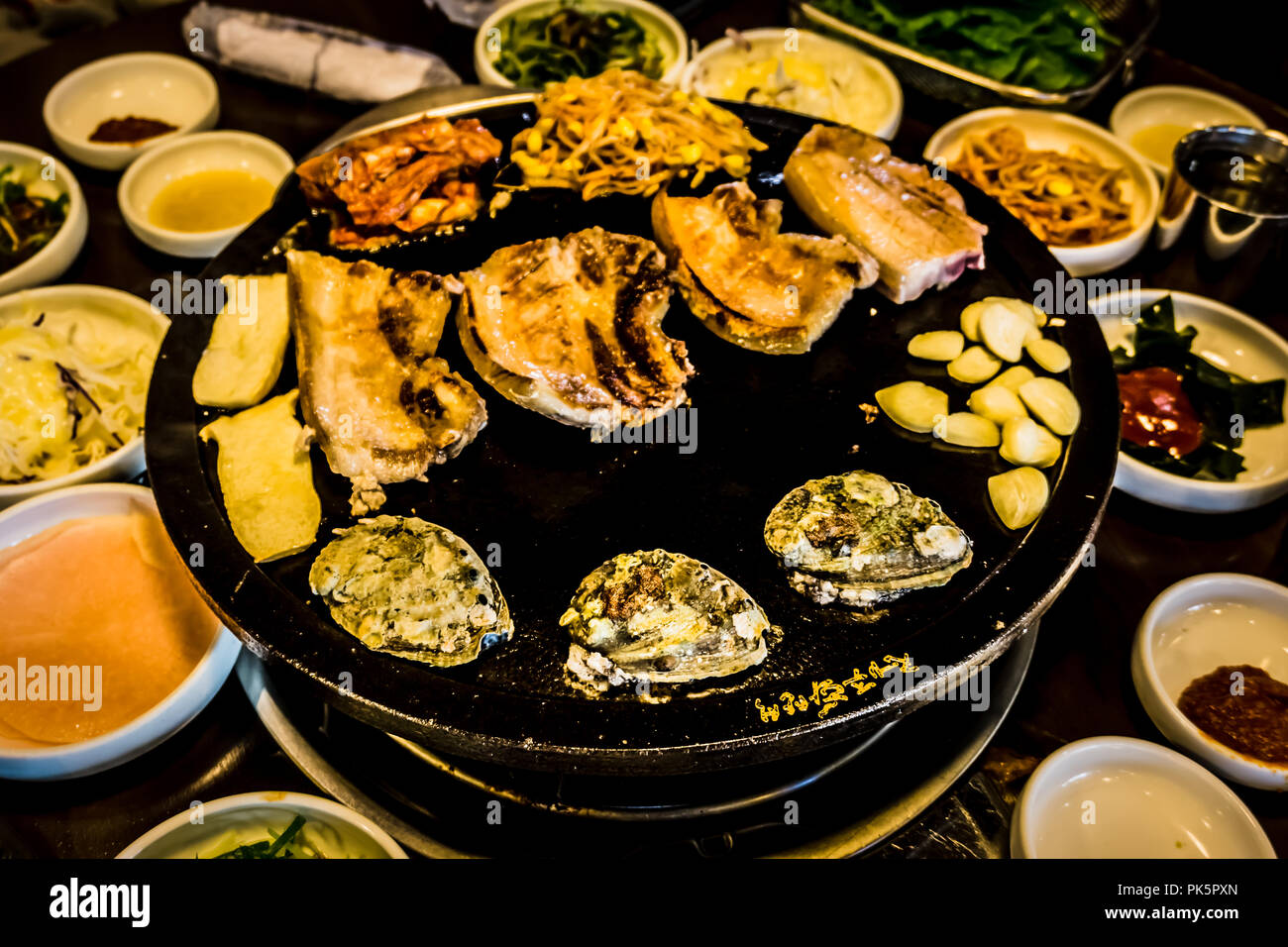 Eating BBQ Black Pork, abalones and side dishes and soup in Black Port Street restaurant in Jeju Island. Stock Photo