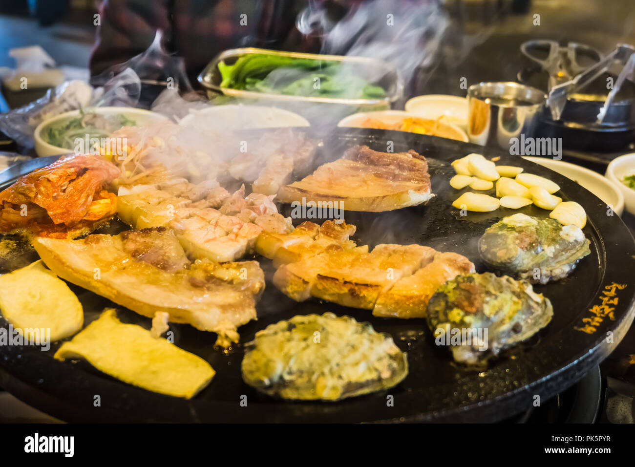 Eating BBQ Black Pork, abalones and side dishes and soup in Black Port Street restaurant in Jeju Island. Stock Photo