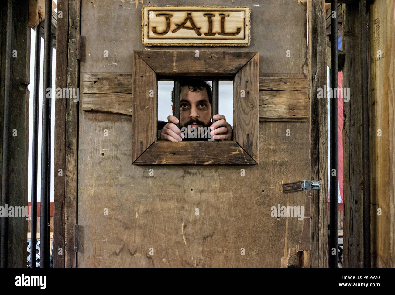 Man with moustache holds the bars of a Jail window as he looks out from his old wooden cell in Dallas-Fort Worth Stock Yards. Horizontal. Stock Photo