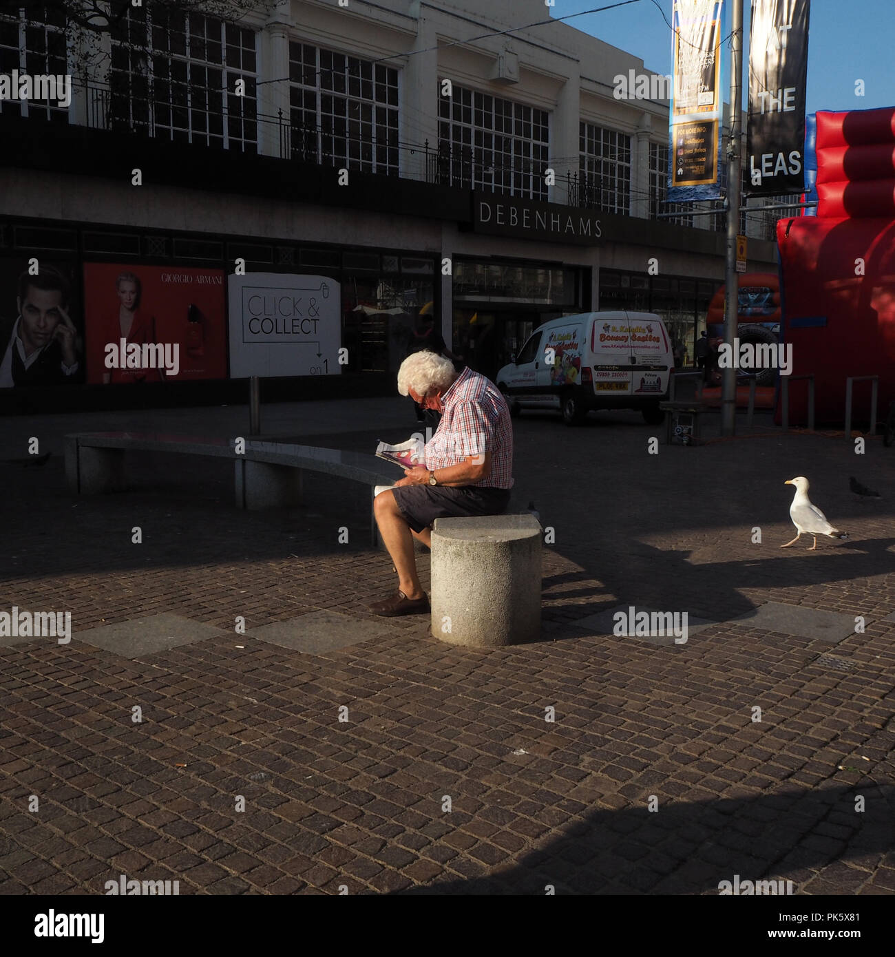 Man reading a newspaper on a seat on the high street Stock Photo