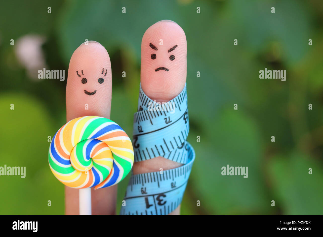 Finger art of couple with meter and candy. Concept of man angry because woman wants to lose weight. Stock Photo