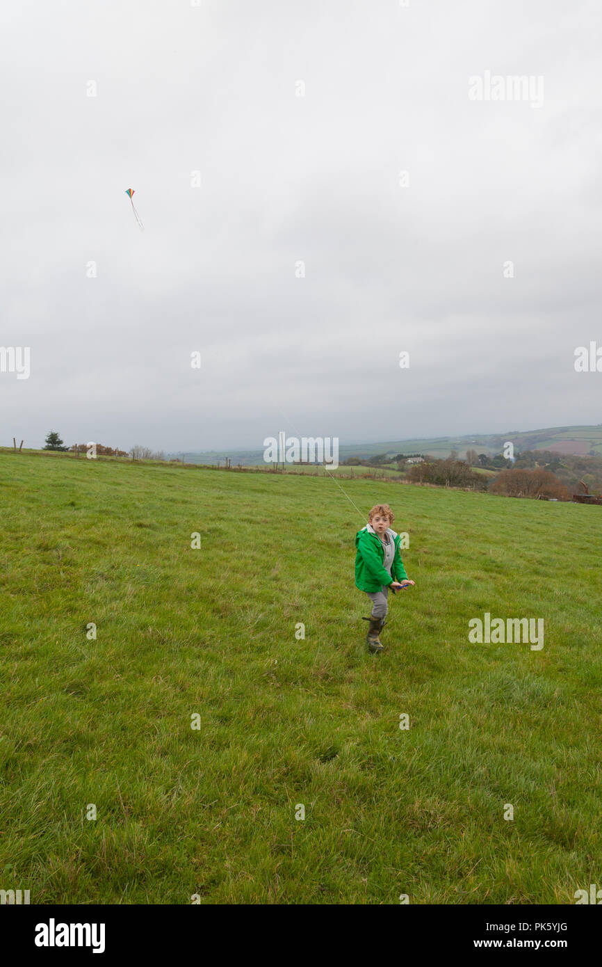 Five year old boy flying a kite in a open field, North Devon, England