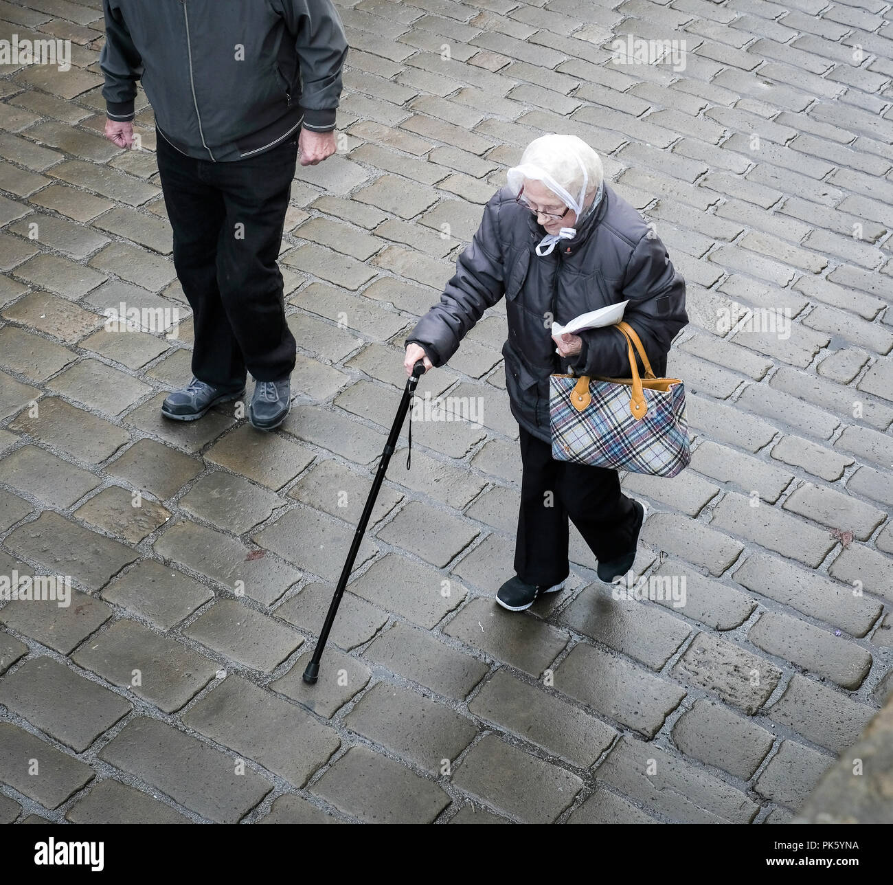 Elderley lady with walking stick over cobbled street Stock Photo