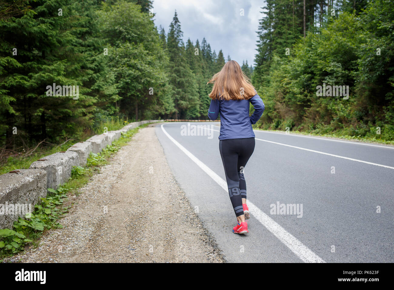 Running girl on the road. Young slim woman jogging in mountains. Rear ...