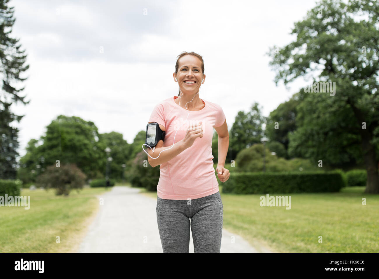 woman with earphones and armband jogging at park Stock Photo