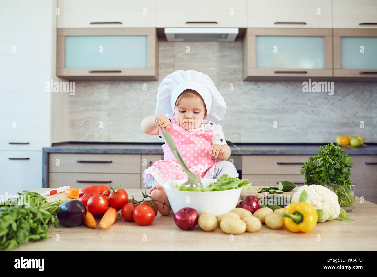 A little girl in a chef's hat prepares  in the kitchen. Stock Photo