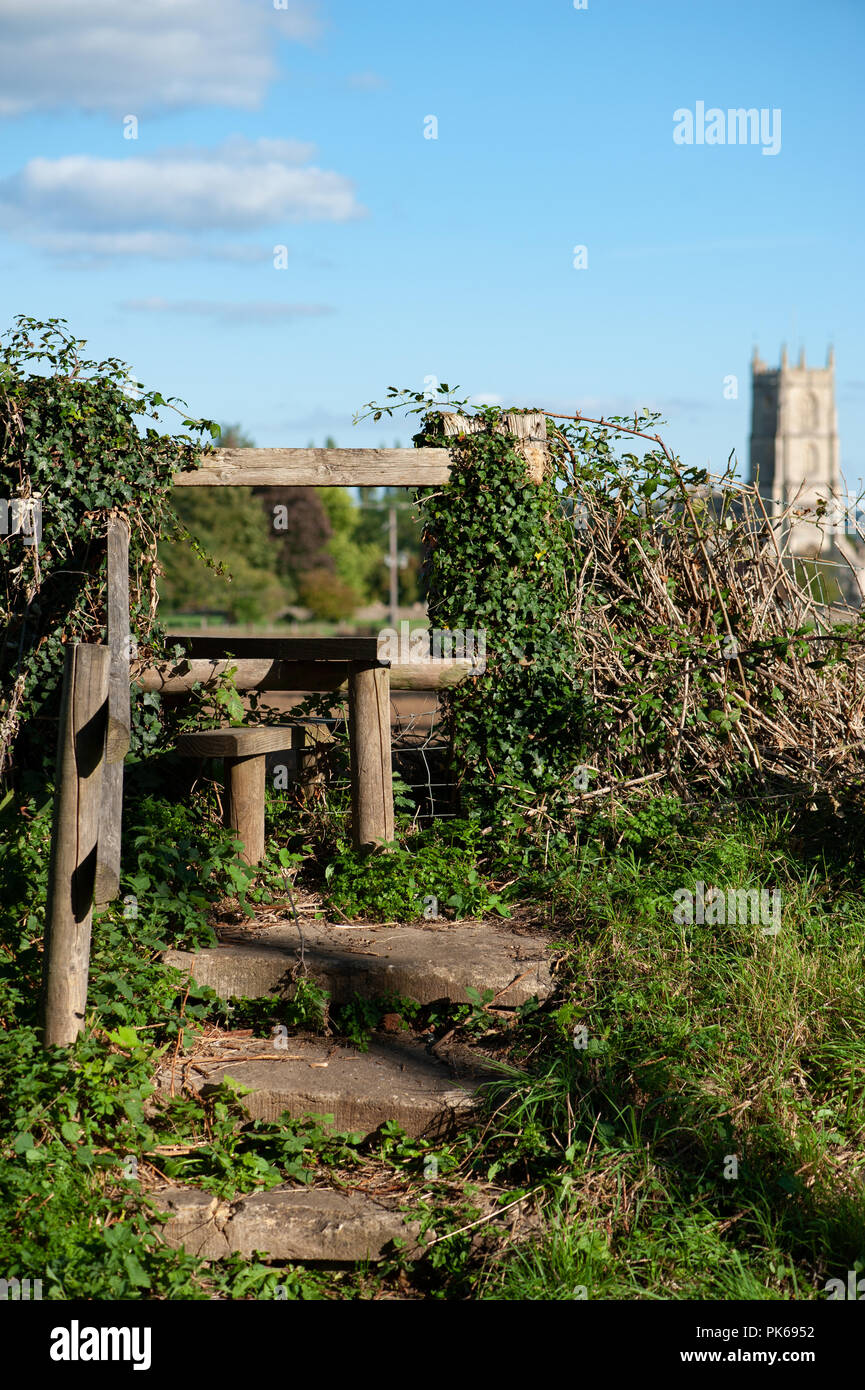 Ivy covered wooden foot stile in Steeple Ashton, Wiltshire, UK showing church steeple in background. Stock Photo