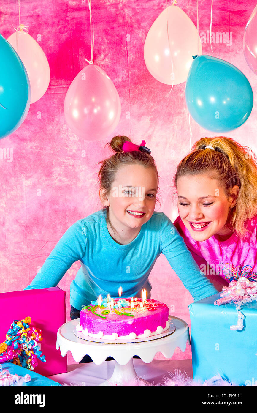 Two beautiful young preteen girls celebrating at a birthday party.  Pink and Aqua balloons and decorations including cake.  Gifts and girls having fun Stock Photo