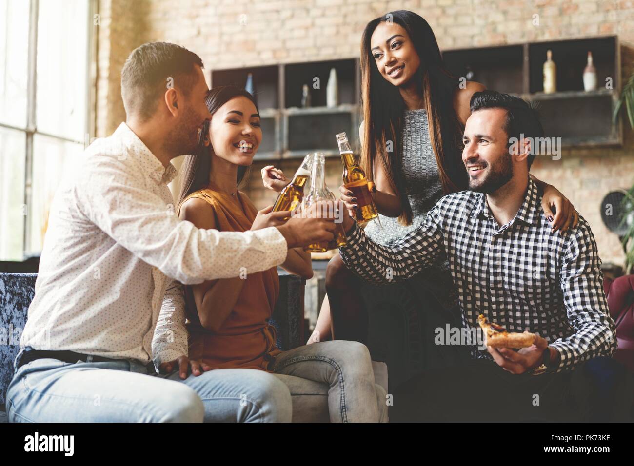 Spending great time with best friends. Group of cheerful young people enjoying food and drinks while spending nice time in cofortable chairs on the kitchen together. Stock Photo