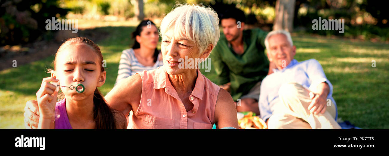 Grand mother looking at her granddaughter blowing bubbles in the park Stock Photo