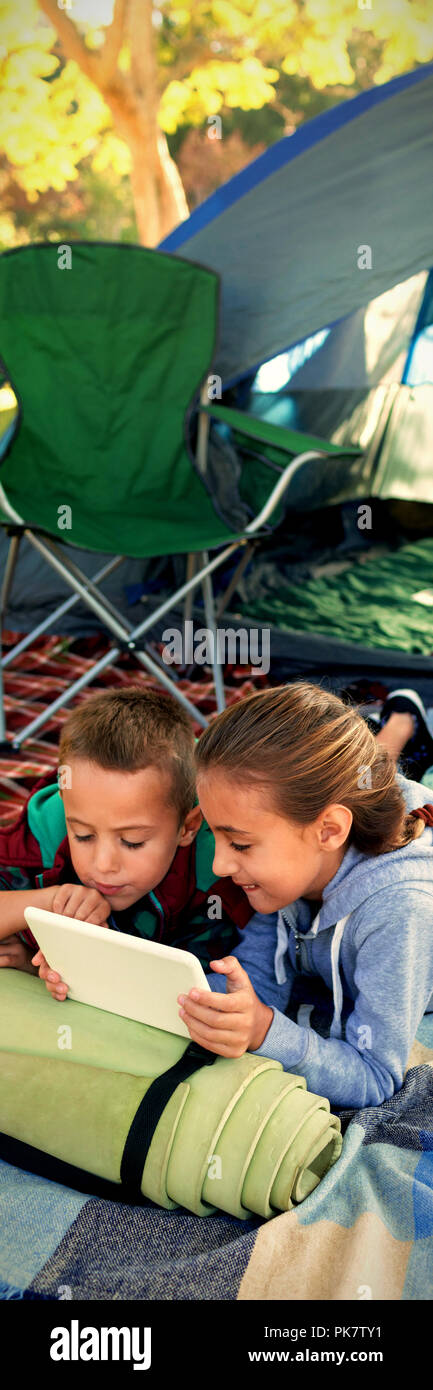 Siblings using laptop outside the tent Stock Photo