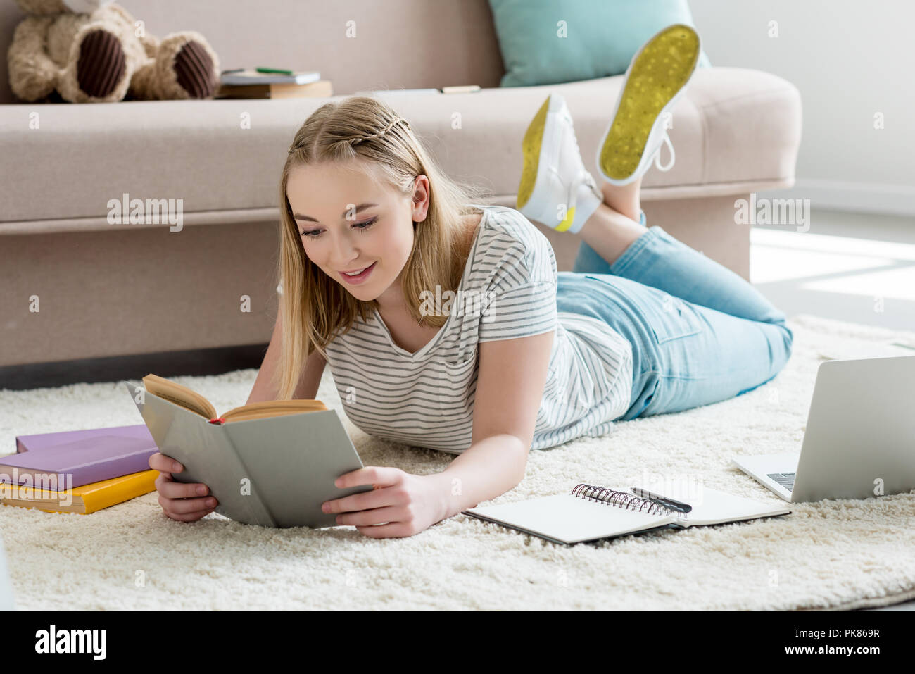 teen student girl reading book while lying on floor Stock Photo