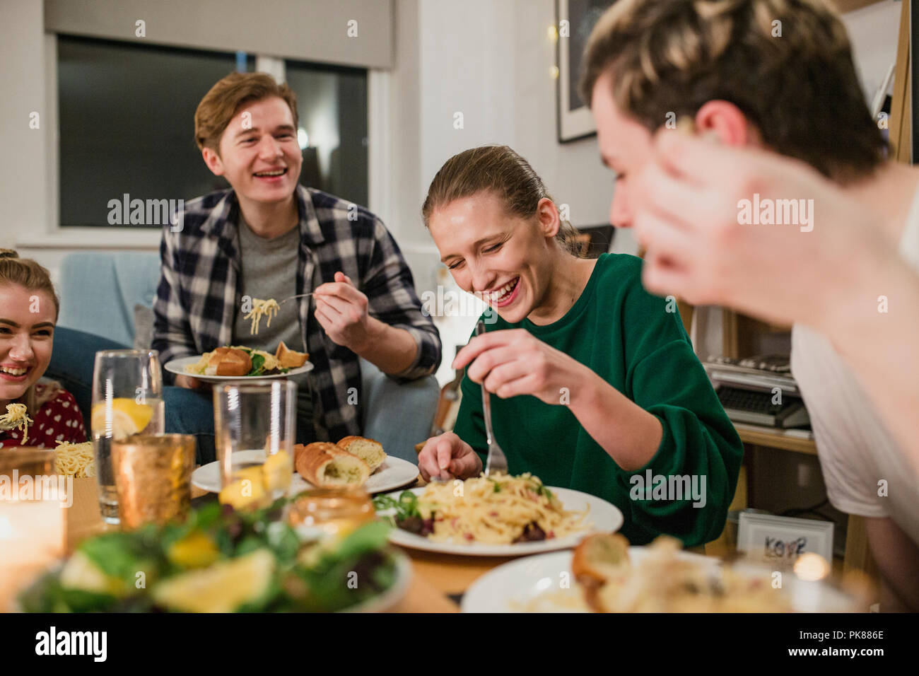 Friends are having a dinner party at home. They are laughing while eating spaghetti carbonara