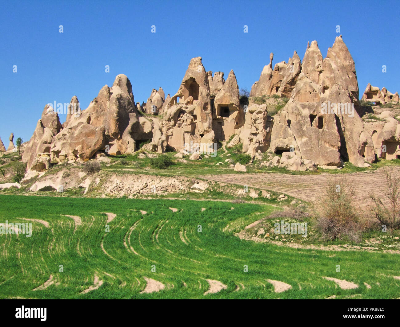 Cave dwellings carved into rock formations with green grass and a blue sky in Goreme Stock Photo
