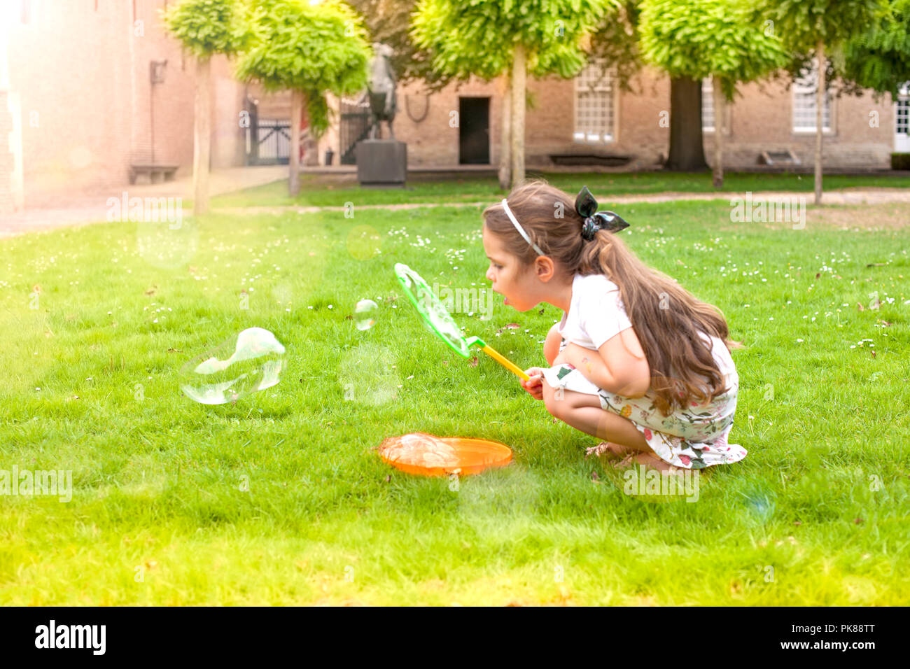 Little girl is playing with soap bubbles in a park on green grass ...