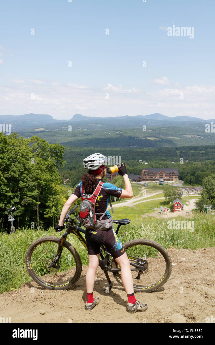 A lady mountain biker (in her 40s) pauses to drink water on the Kingdom Trails mountain bike park in East Burke, Vermont, USA Stock Photo