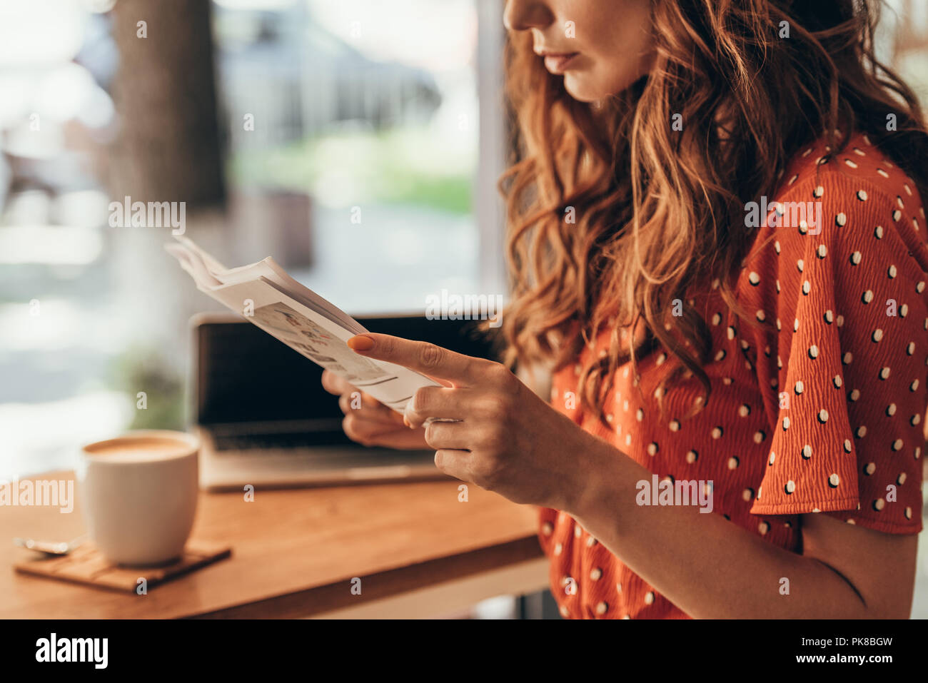 partial view of woman reading newspaper at table with laptop in coffee shop Stock Photo
