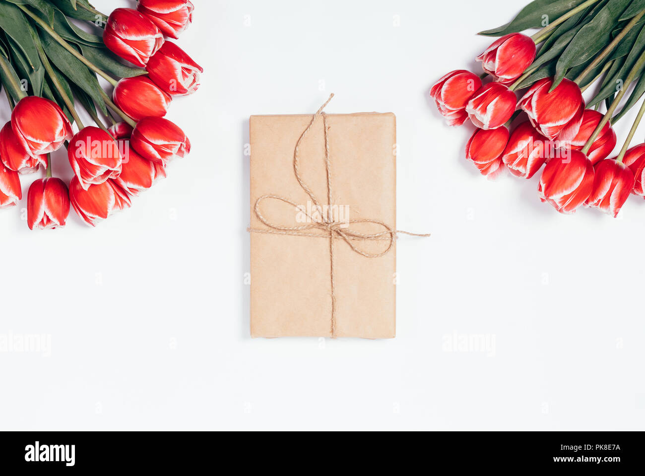 Gift box tied with jute rope between blooming red flowers on white ...