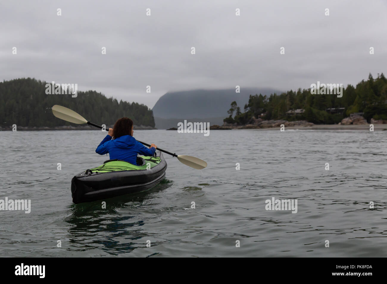 Girl kayaking in the ocean during a cloudy and gloomy sunrise. Taken in