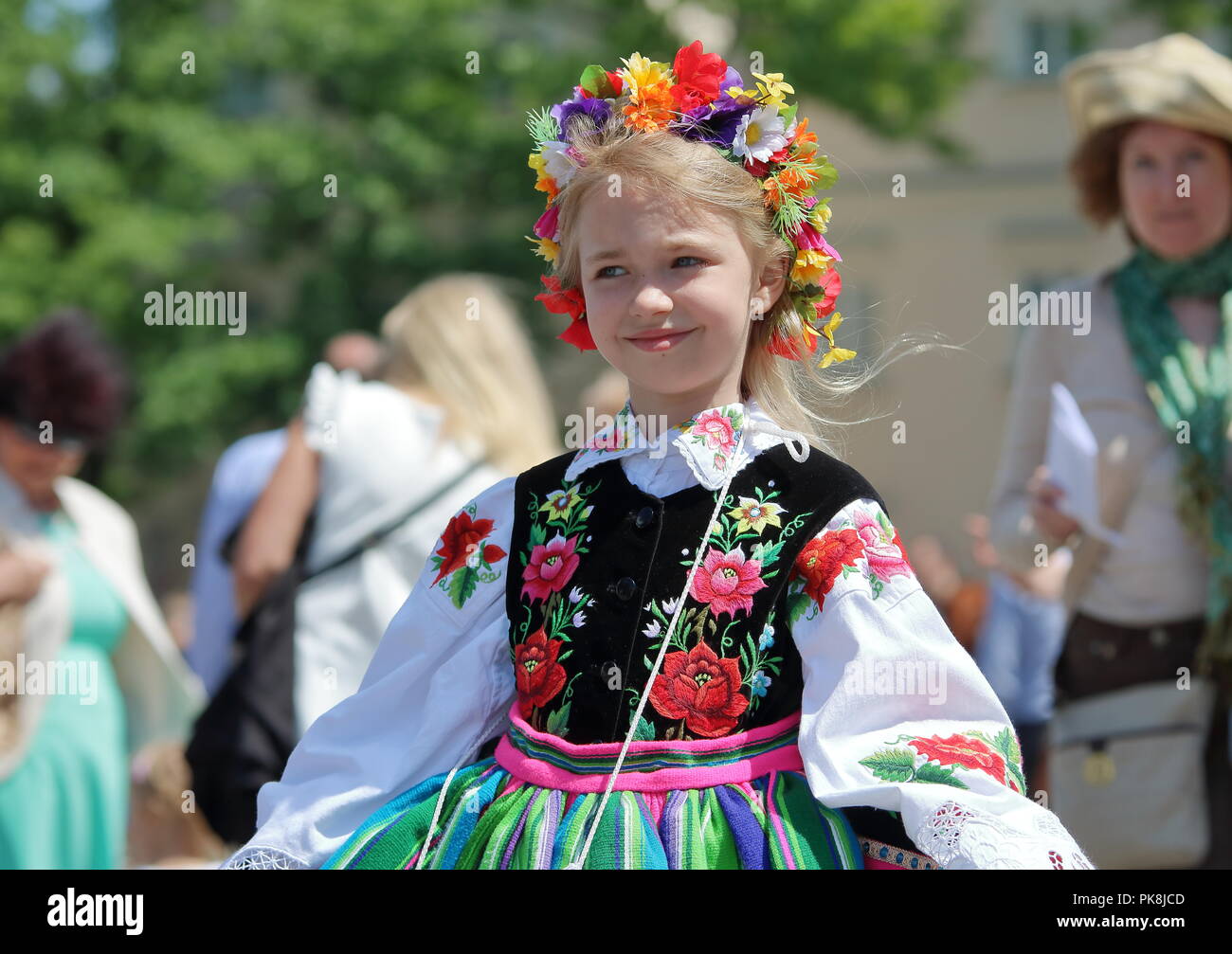 two girls dressed in traditional regional folk costumes from Lowicz region,  Poland, on square, show colorful striped skirts, Stock Photo