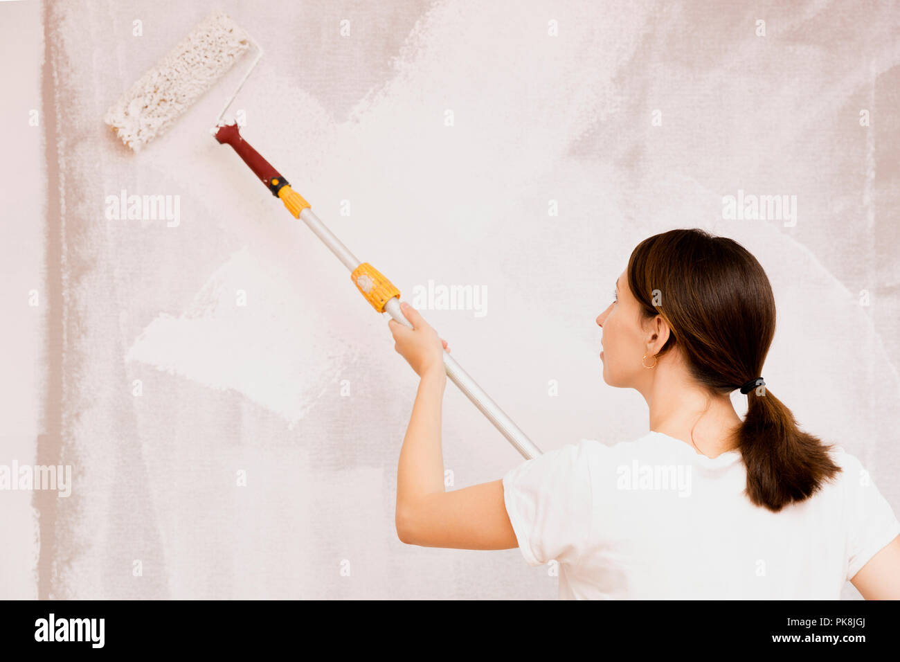 Home improvement. Beautiful woman painting wall with paint roller. Stock Photo