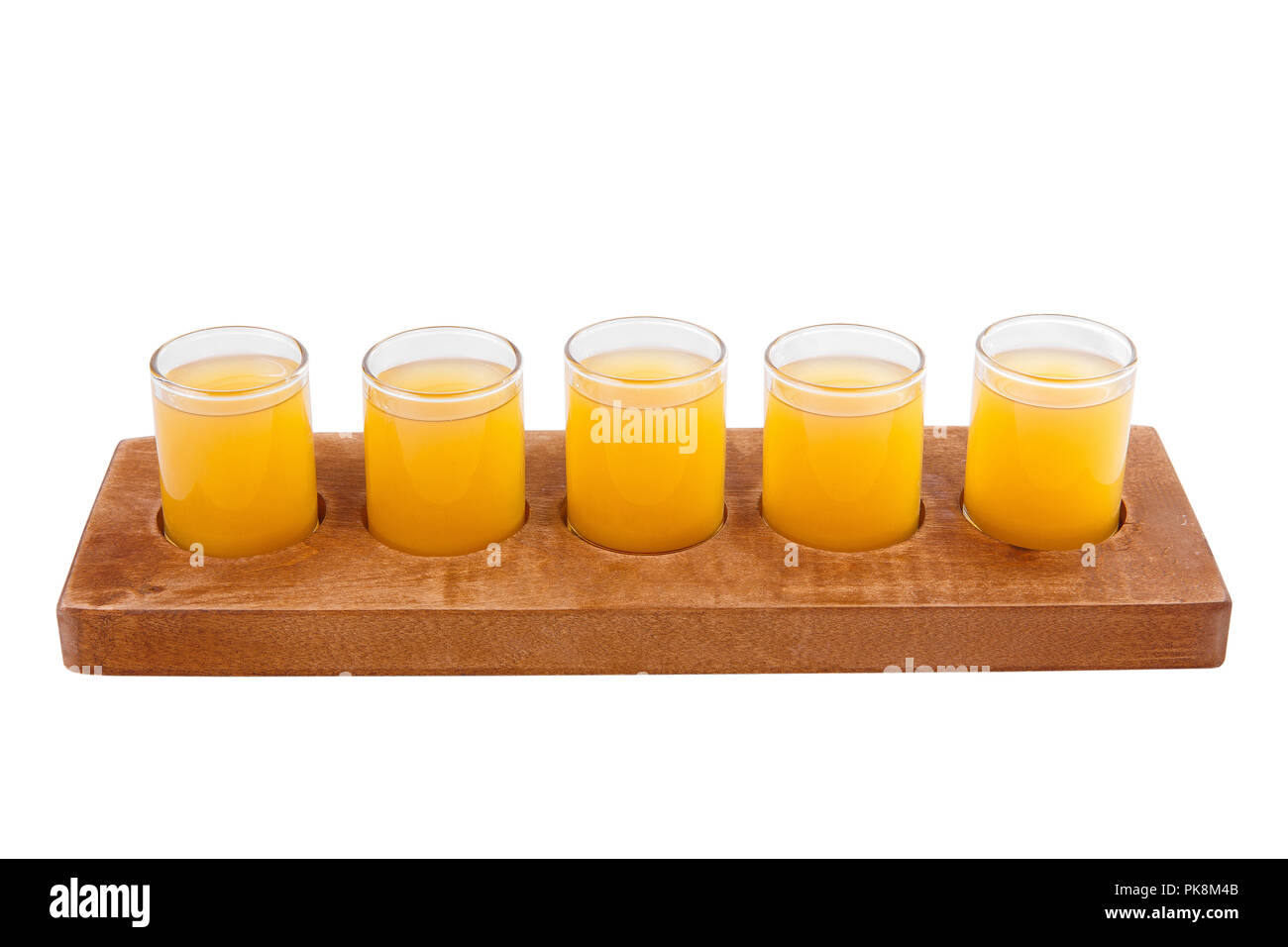 Yellow, same color opaque cocktails, a set of shots in one row, five servings on a wooden stand, substrate. Side view Isolated white background. Drink Stock Photo