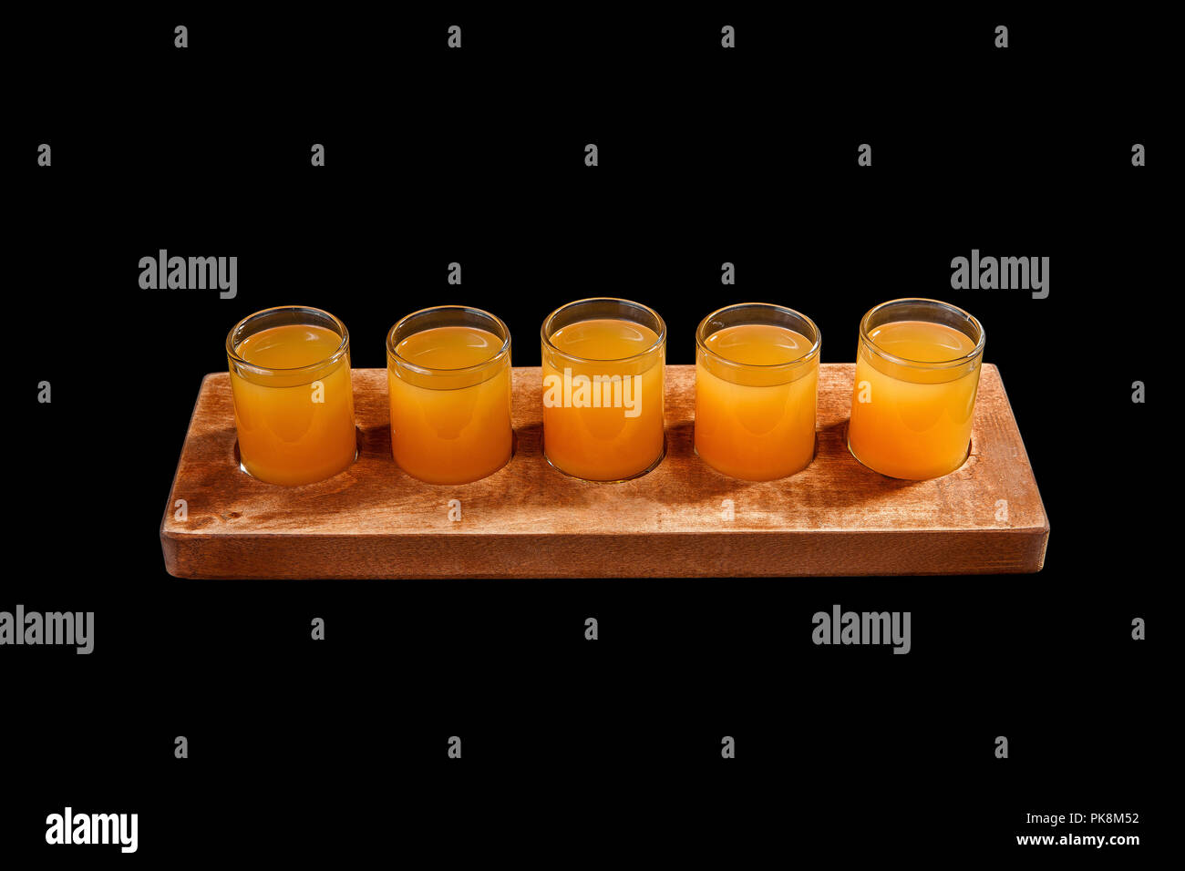 Yellow, same color opaque cocktails, a set of shots in one row, five servings on a wooden stand, substrate. Side view Isolated black background. Drink Stock Photo