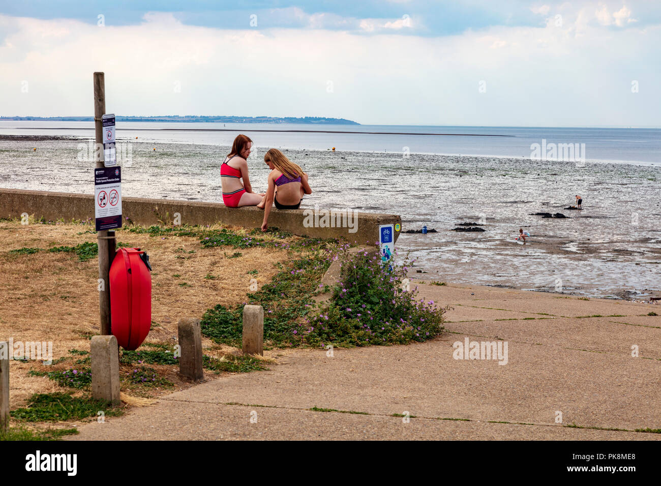 Teenage girls sit on a wall and chat on an early summer afternoon at the start of the school holidays, Hampton, Herne Bay, Kent, UK Stock Photo