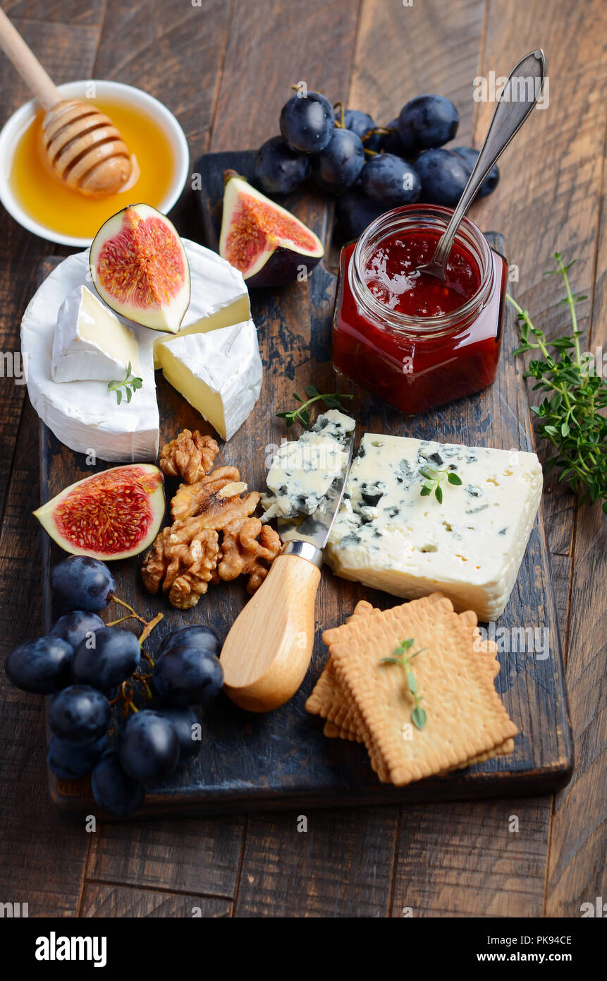 Cheese plate with grapes, figs, crackers, honey, plum jelly, thyme and nuts, selective focus. Stock Photo