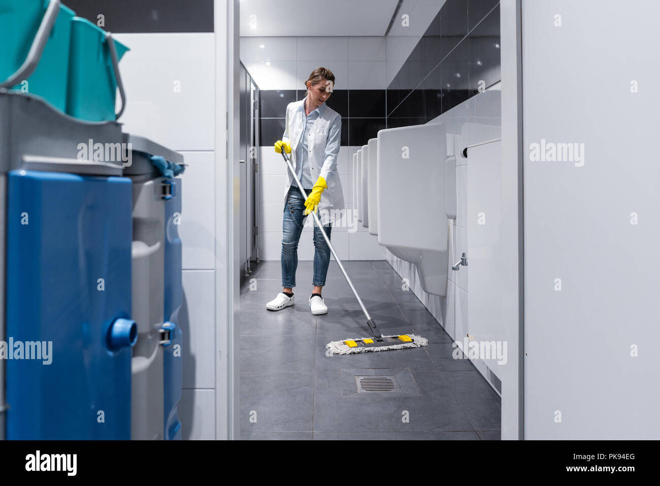 Cleaning lady mopping the floor in mens restroom Stock Photo