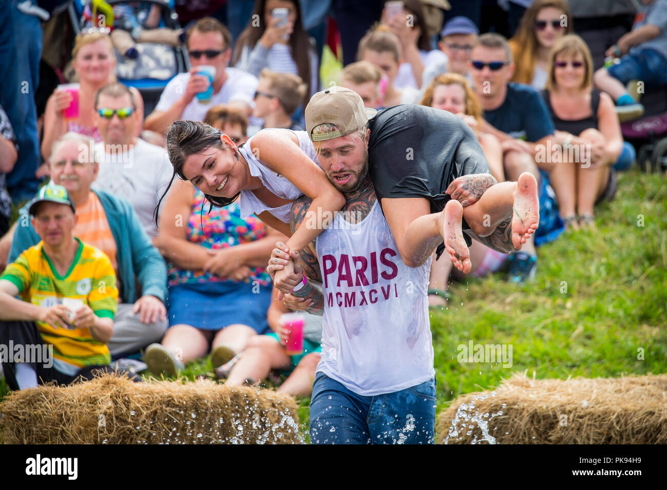 Man carrying a woman over a dirty and wet obstacle course at The Lowland Games in Thorney, Somerset, England Stock Photo