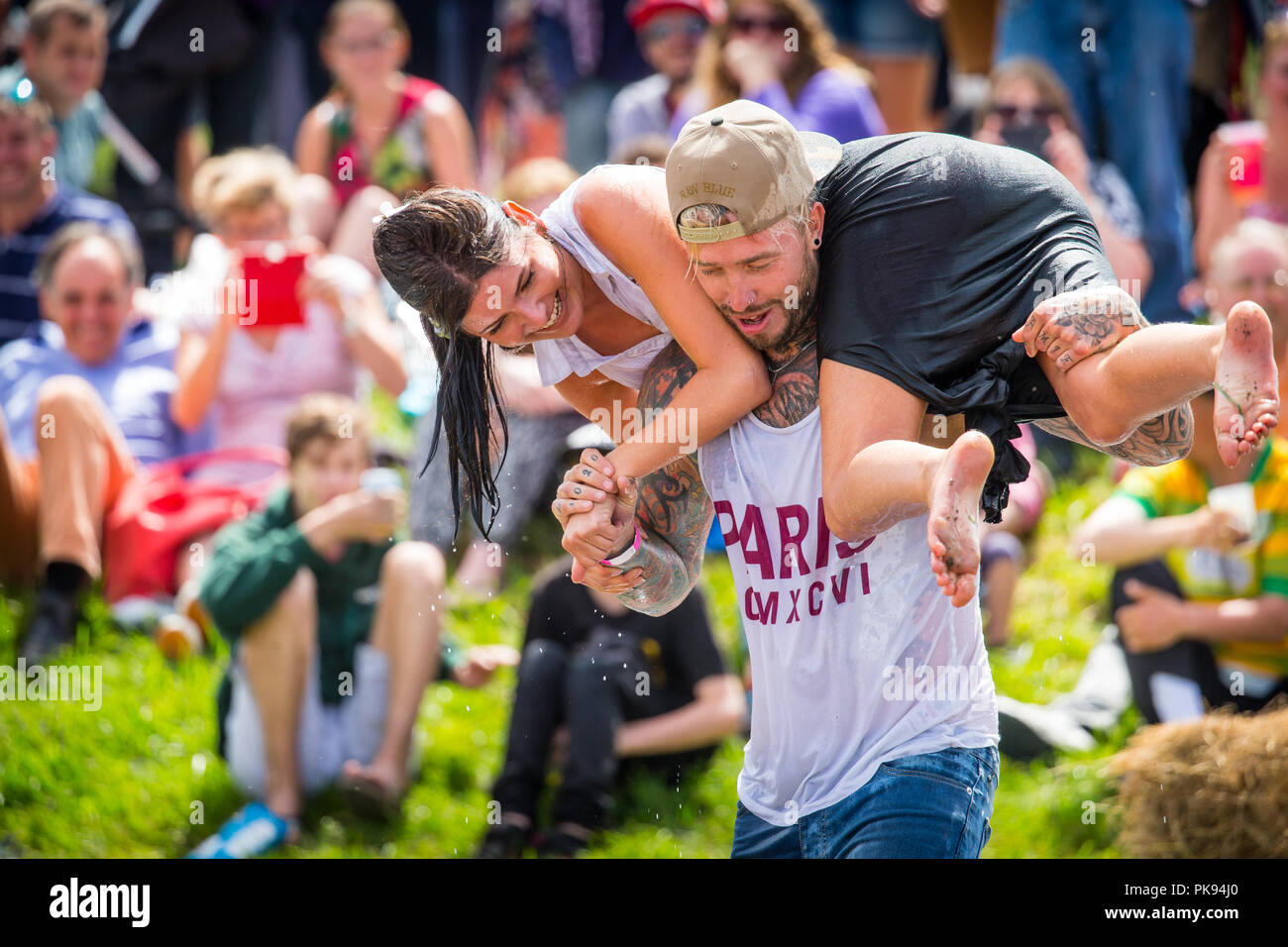 Man carrying a woman over a dirty and wet obstacle course at The Lowland Games in Thorney, Somerset, England Stock Photo