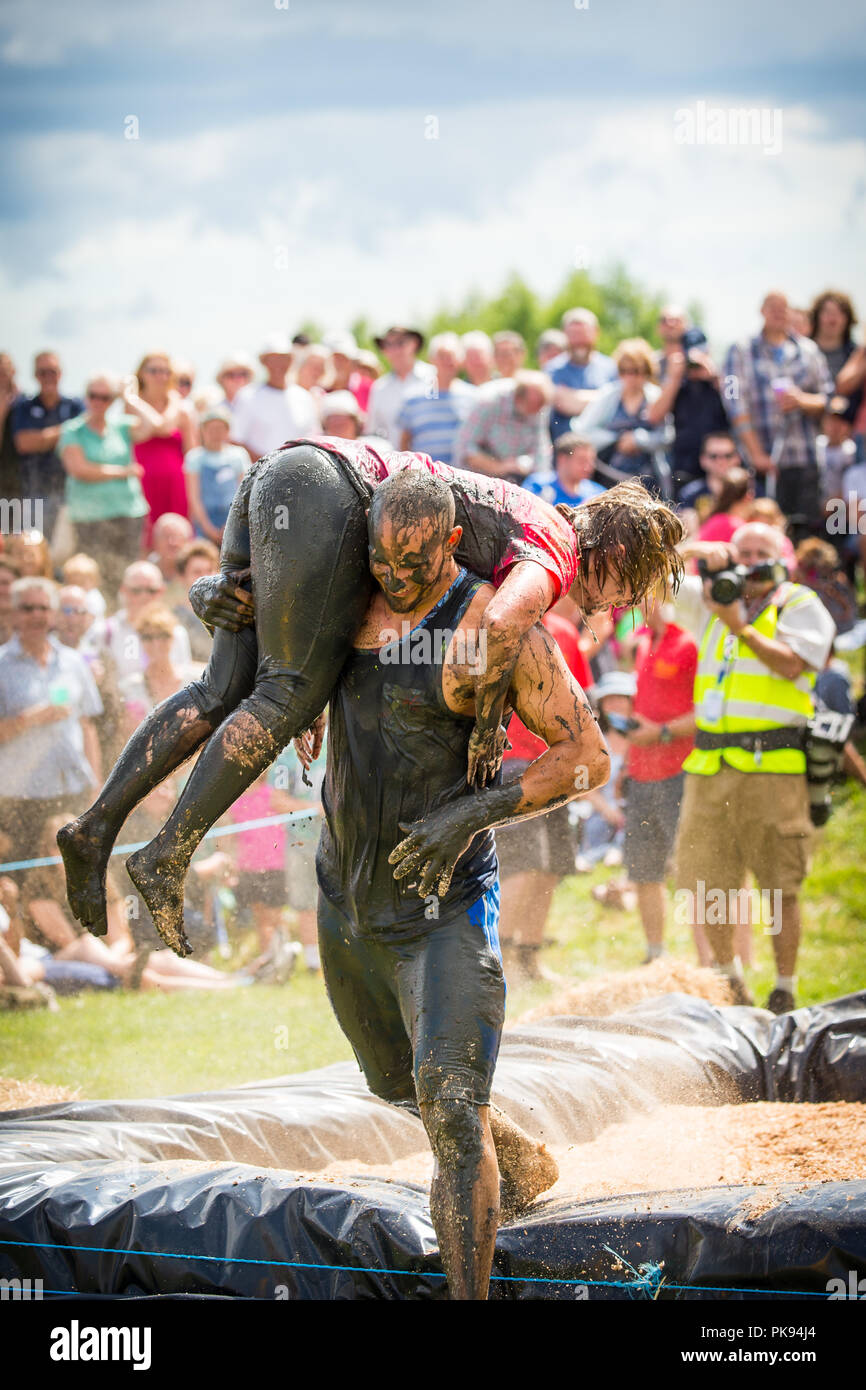 Man carrying a woman over a dirty and wet obstacle course at The Lowland Games in Thorney, Somerset, England Stock Photo